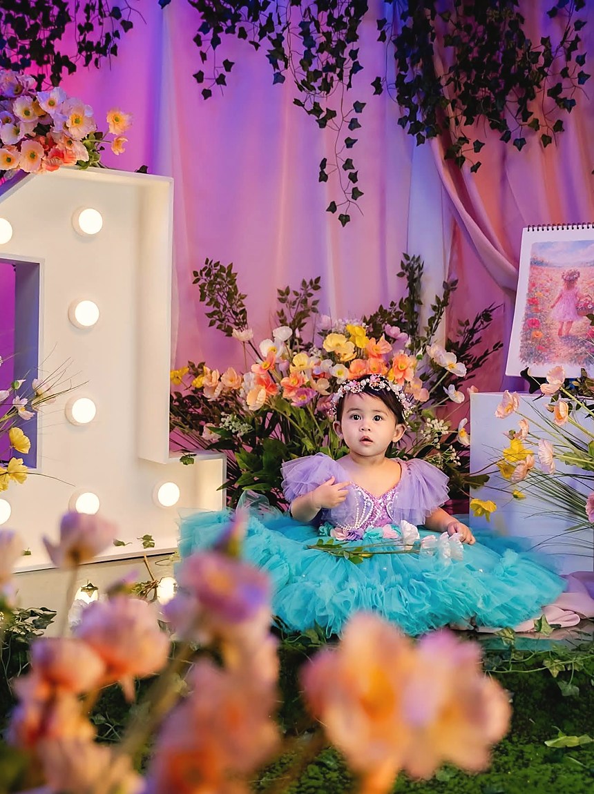 A first birthday in an enchanted garden setting, a lit numeral one beside a bank of pastel flowers