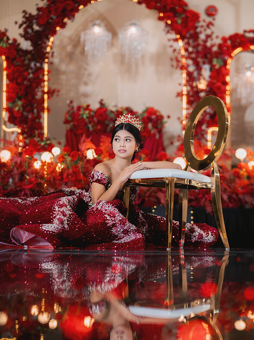 A debutante seated beside a gold chair on a red mirrored stage