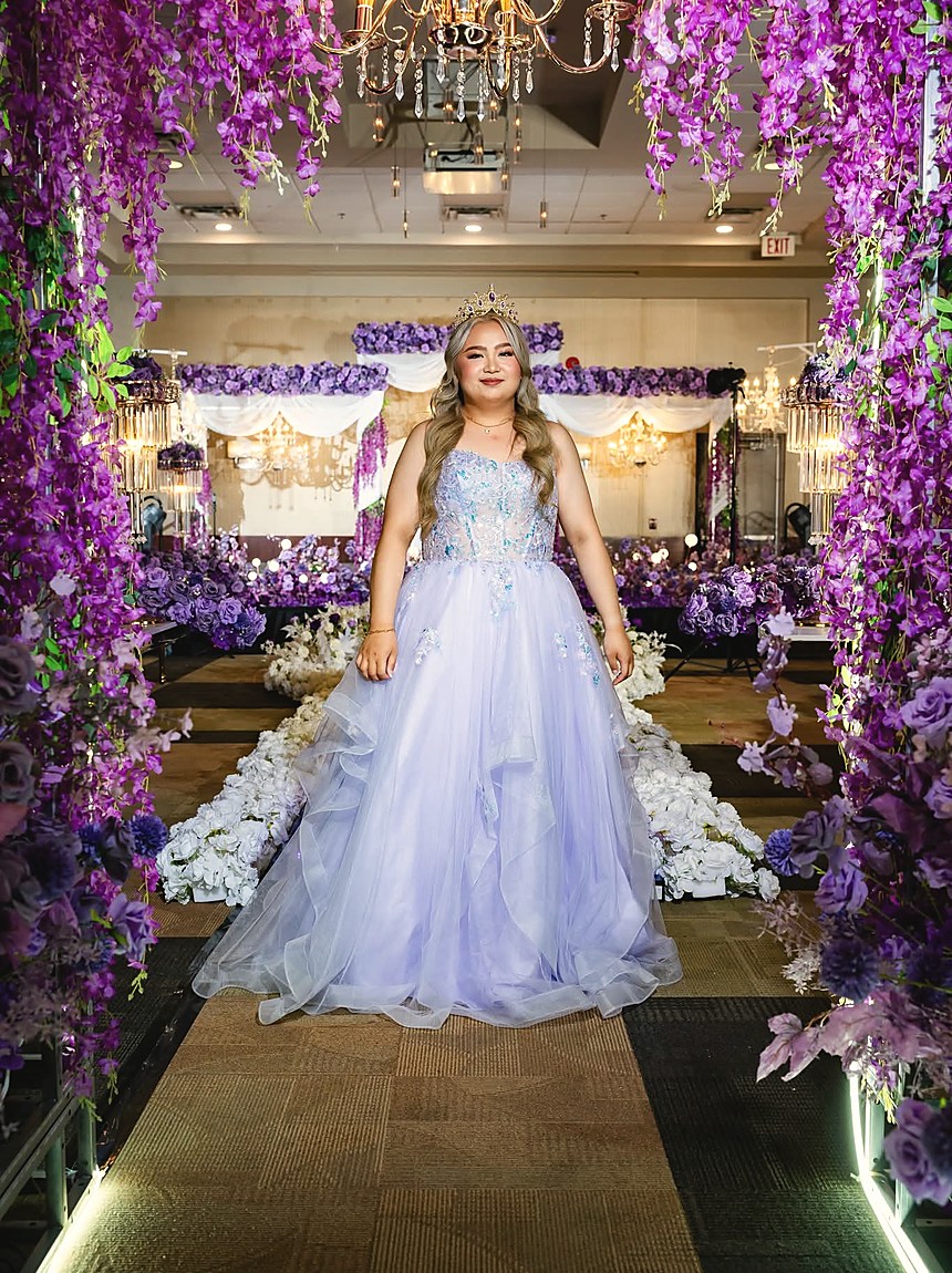A debutante in a lilac gown descending a staircase framed by purple wisteria