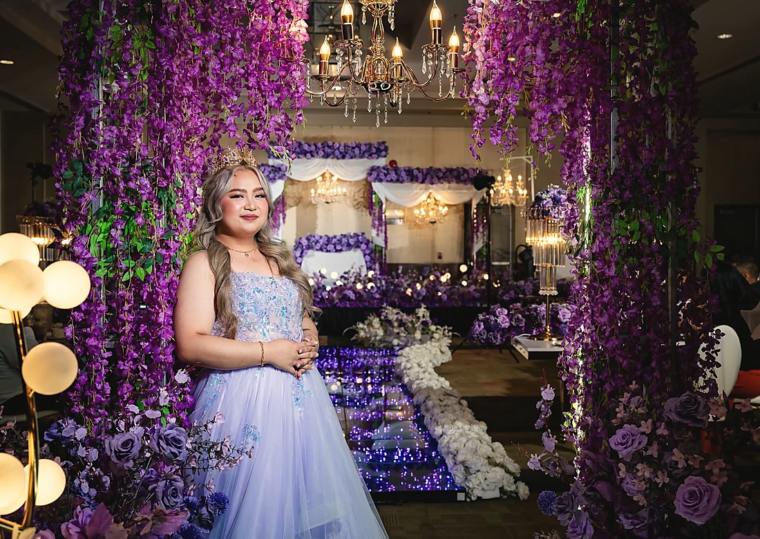 A debutante standing in a corridor of hanging purple blooms