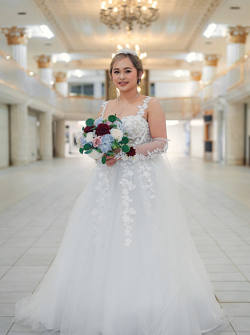 A bride walking a bright corridor holding a red and white bouquet