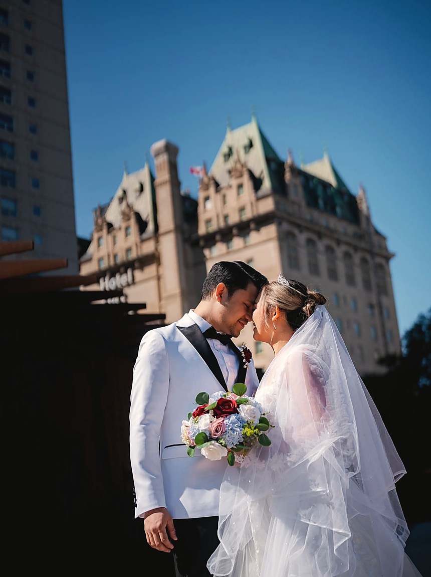 A bride and groom about to kiss outside a stone hotel at dusk