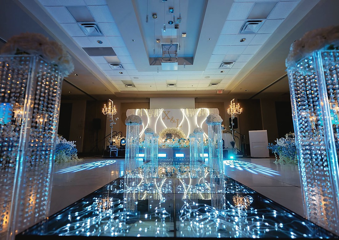 A mirrored dance floor lit blue beneath a white floral arch