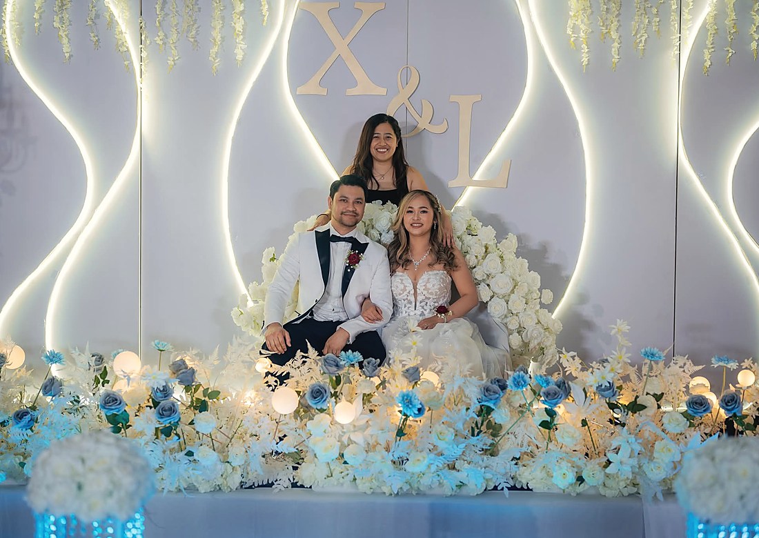 A couple seated on a floral stage beneath an illuminated monogram