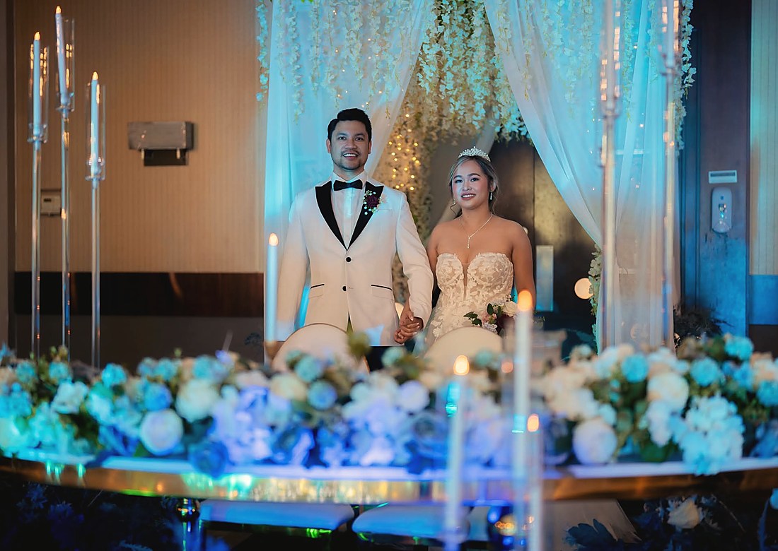 A couple on a candlelit stage under a draped floral canopy