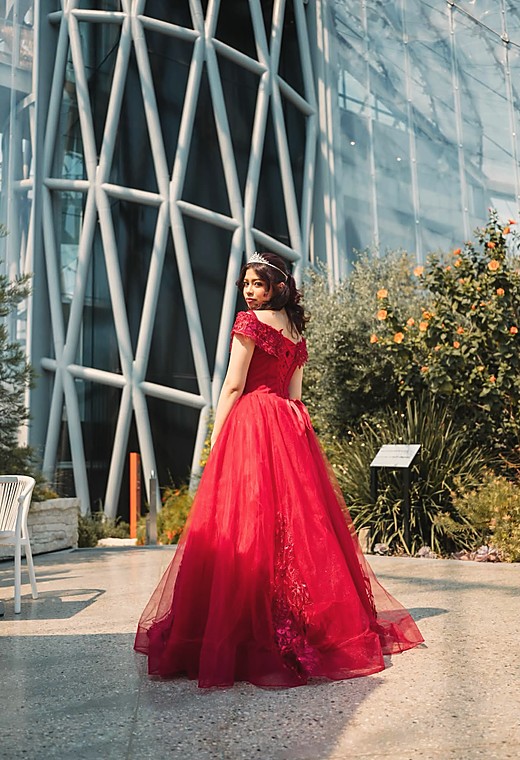 A debutante in a red ball gown outside a glass fronted building