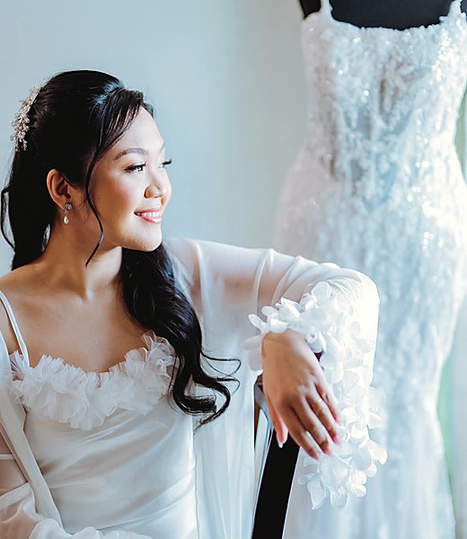 A bride in a lace gown resting against her dress at the window