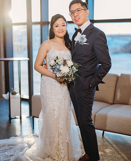A bride and groom standing together, her winter bouquet between them